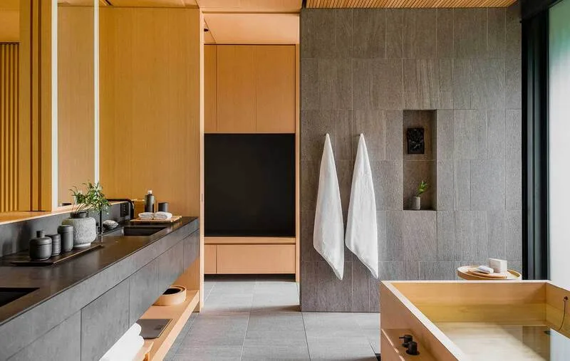 Phòng tắm Japandi kết hợp đá trung tính, gỗ chống ẩm và ánh sáng vàng nhẹ để tạo cảm giác thư thái.